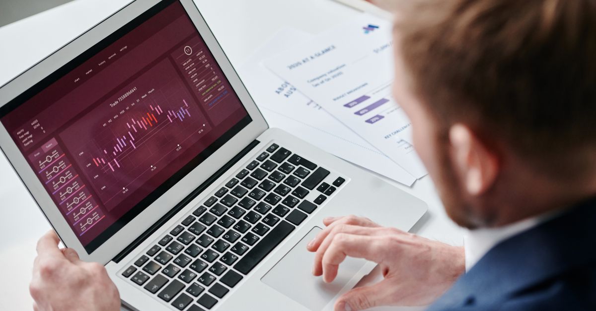 A trader reviewing a trading dashboard on a laptop showing a candlestick chart and performance figures.