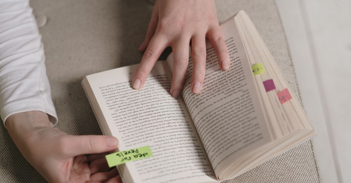 An up-close view of hands holding an open book with colorful bookmarks, ideal for literary themes.