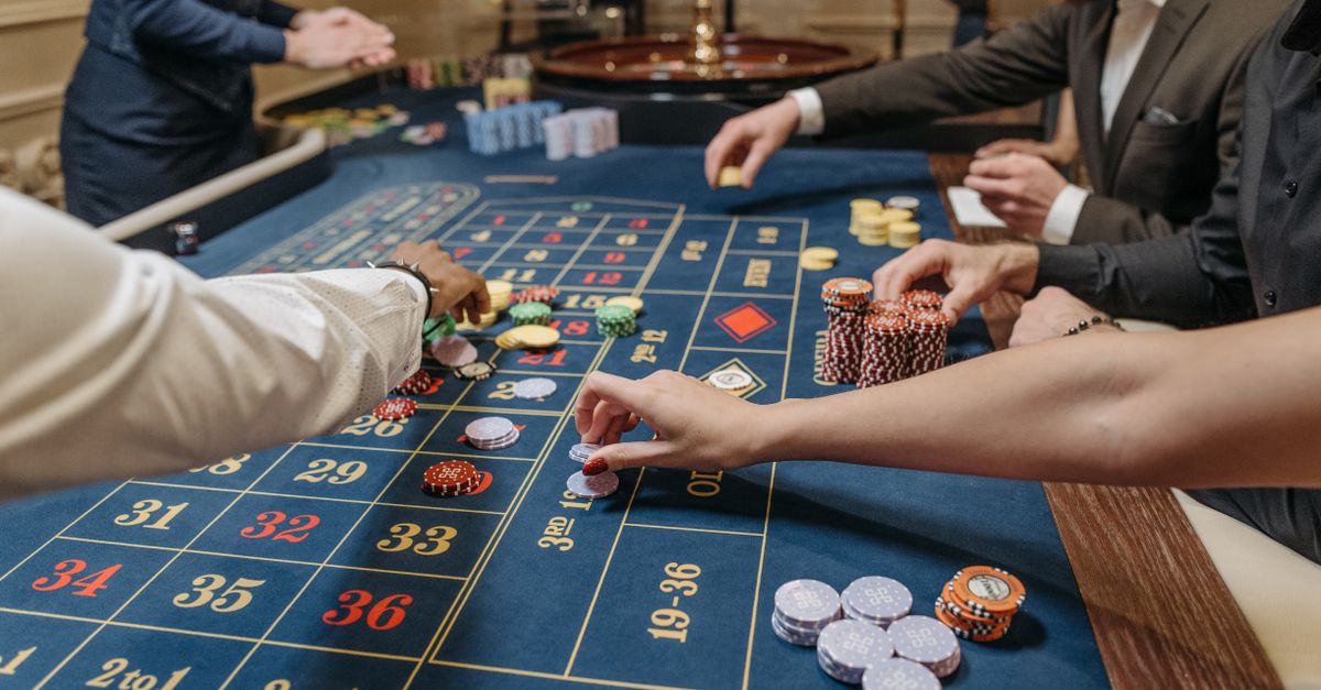 A lively casino scene with players placing bets and handling gaming chips on a roulette table.